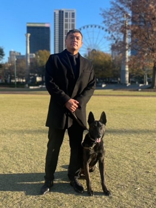 handler and his dog in a park with tall buildings behind them.
