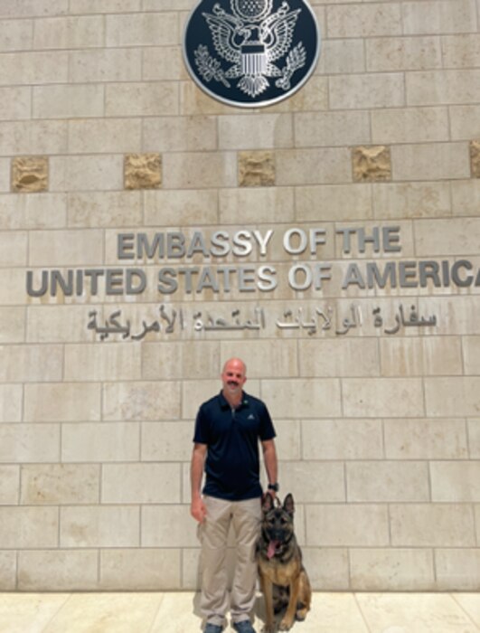 handler and his dog in front of an embassy building
