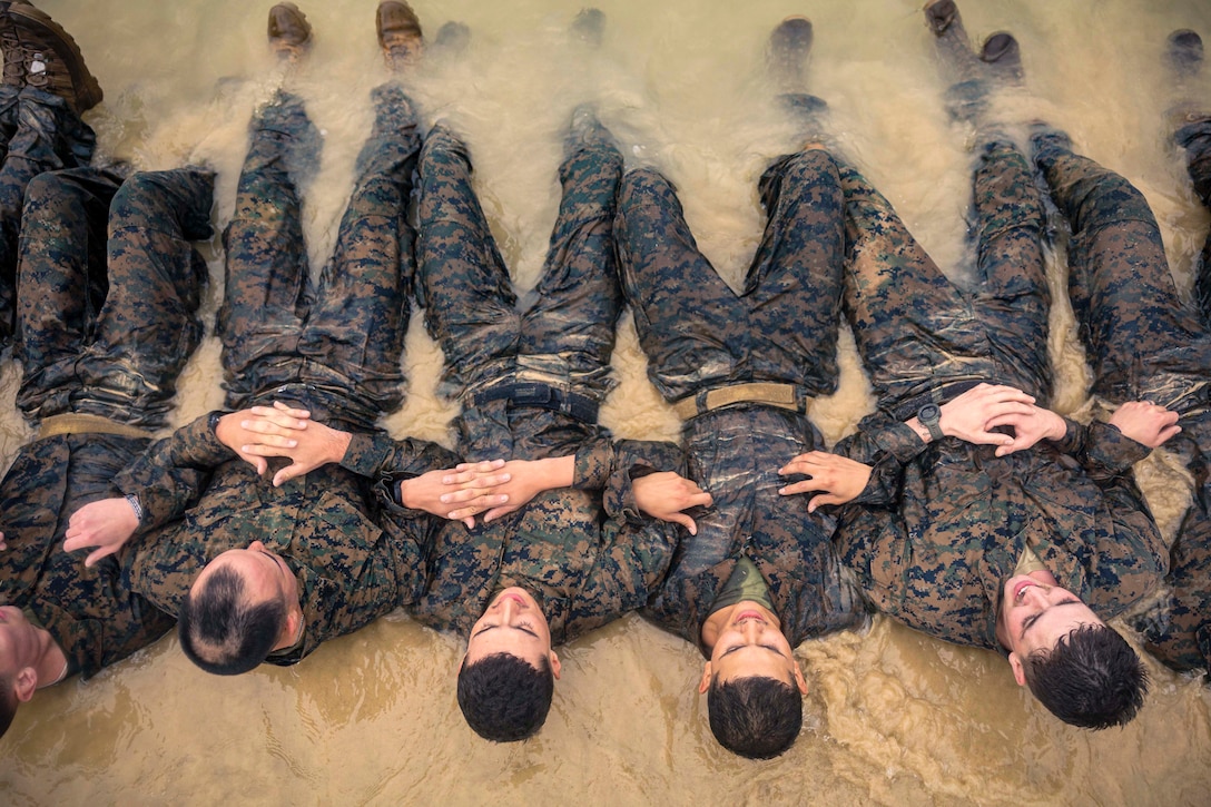 Marines lock arms while performing situps in muddy waters as seen from above.