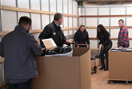 Five people sort through laptop and accessories in a trailer.