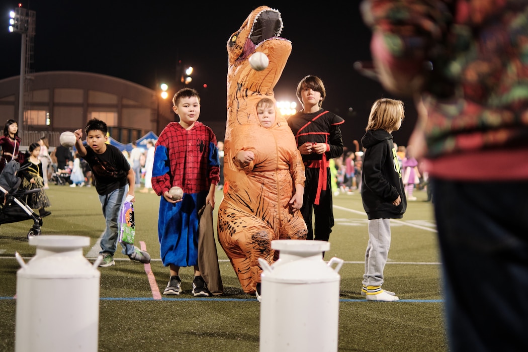 Boy dressed as a dinosaur tosses ball at a carnival game in Yokosuka, Japan on Halloween.