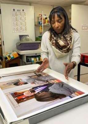 A woman in a white top looks down on a photo print to two people.