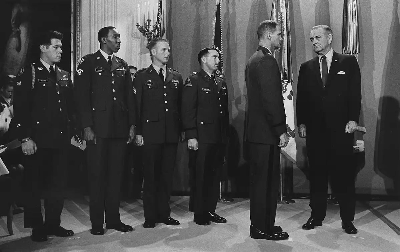 Four men stand in a row, looking toward two other men who are looking face-to-face.