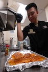 Senior Airman Matthew Chan, 5th Force Squadron food service specialist, tops a chicken breast with seasoning at Missile Alert Facility Oscar, North Dakota, Dec. 21, 2023. A missile chefs’ duties at a MAF include completing and stocking inventory as well as preparing, cooking and cleaning after each mealtime. (U.S. Air Force photo by Senior Airmen Alexander Nottingham)