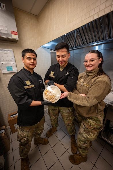 Senior Airman Alexander Guidry, Airman 1st Class Oscar Vega and Senior Airman Matthew Chan, 5th Force Support Squadron food service specialists, pose with a prepared meal at Missile Alert Facility Oscar, North Dakota, Dec. 21, 2023. During their deployment, missile chefs can make 20 to 40 meals a day for the Airmen stationed on site. (U.S. Air Force photo by Senior Airmen Alexander Nottingham)