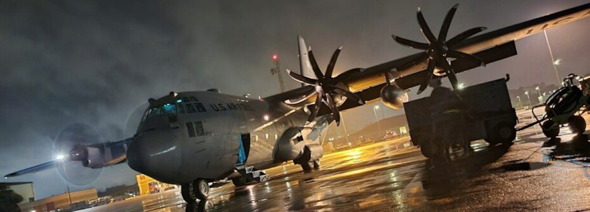 a C-130 is parked on a flightline during the rain