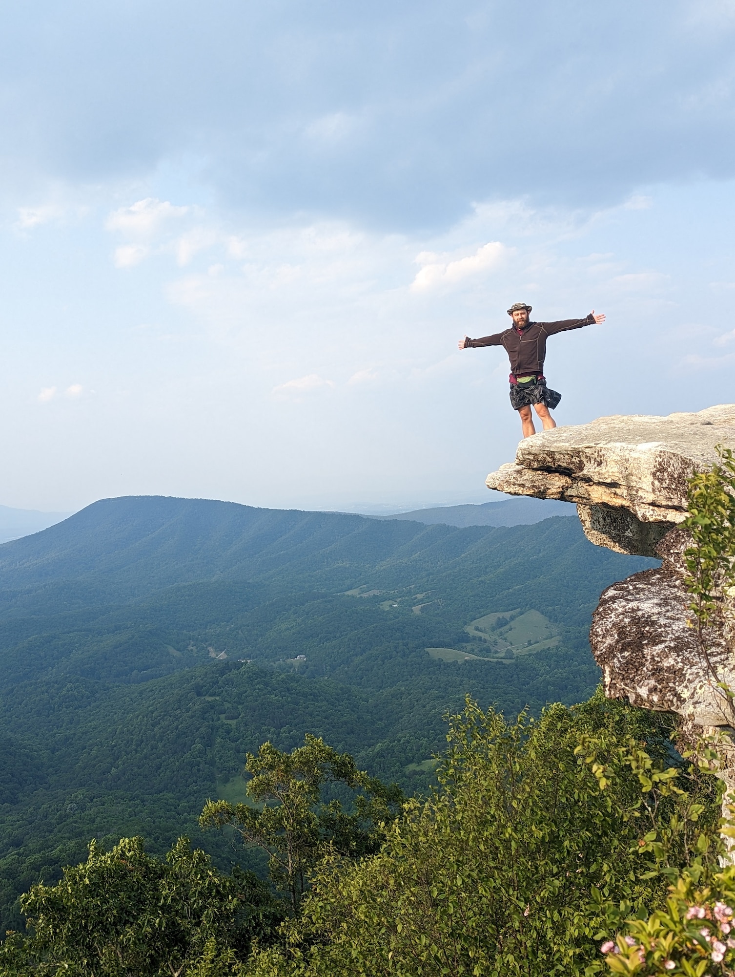 Airman stands on cliff with mountains in the background.