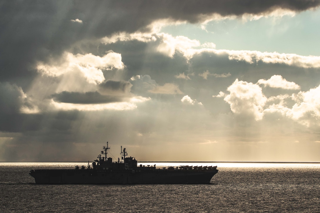 A large military ship sails on the water at twilight.