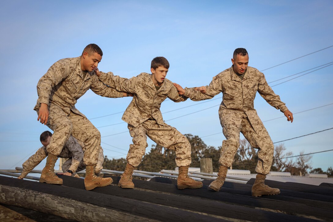 Three people lock arms as they walk across round poles.