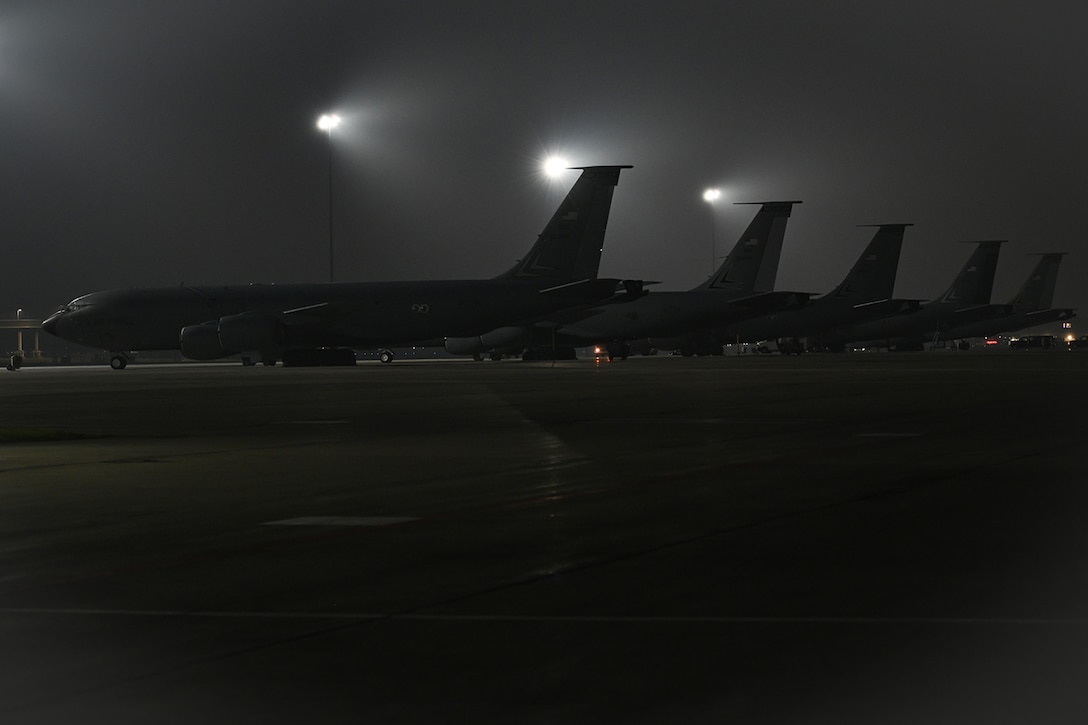 Five military aircraft are parked on the tarmac on a cloudy night.