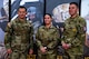 Two male and one female Soldier in uniform pose together in front of Army recruiting banner-ups