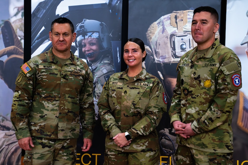 Two male and one female Soldier in uniform pose together in front of Army recruiting banner-ups