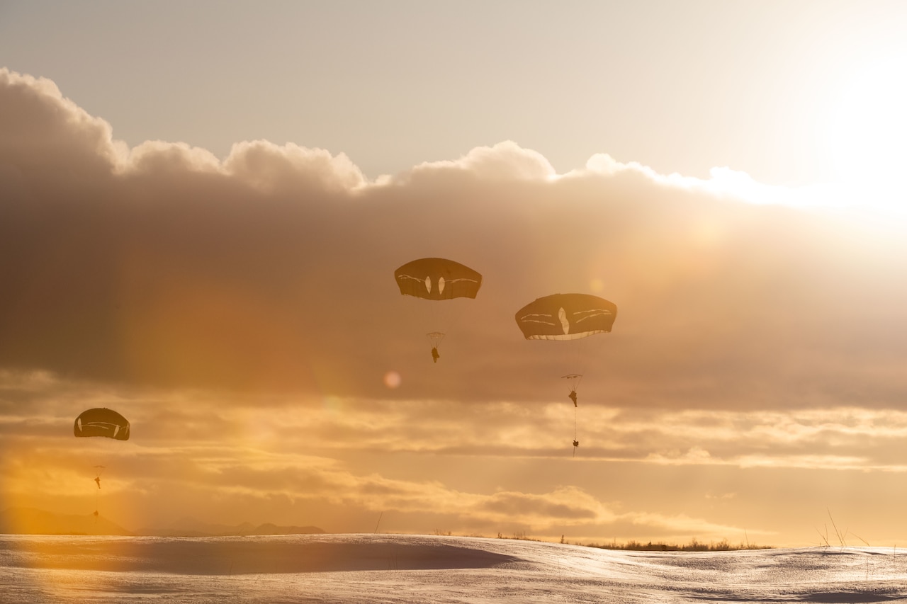 Soldiers descend with parachutes under a sunlit sky.