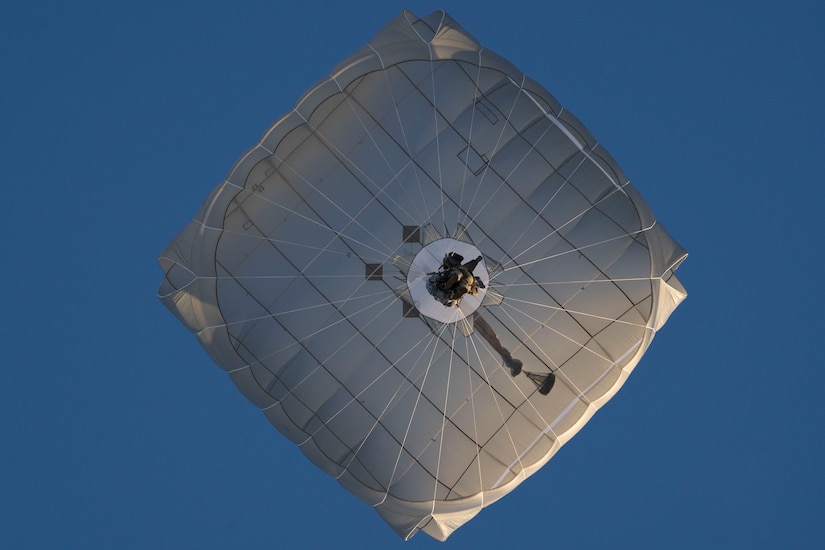 A soldier descends with a parachute as seen from below.