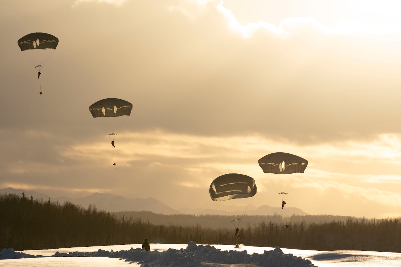 Soldiers descend with parachutes under a sunlit sky.