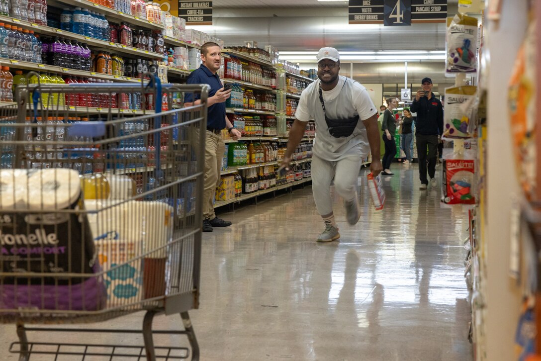 Petty Officer 2nd Class Kaleb Burrell, a religious program specialist with the Chaplains Religious Enrichment Development Program, Marine Corps Installations Pacific, races to throw groceries in his shopping cart during the Camp Foster Commissary Shopping Spree Contest at the commissary on Camp Foster, Okinawa, Japan, Dec. 13, 2023. Camp Foster Commissary partnered with Military AutoSource to grant 4 individuals a total of $1,000 to spend in a time limit. (U.S. Marine Corps photo by Cpl. Thomas Sheng)