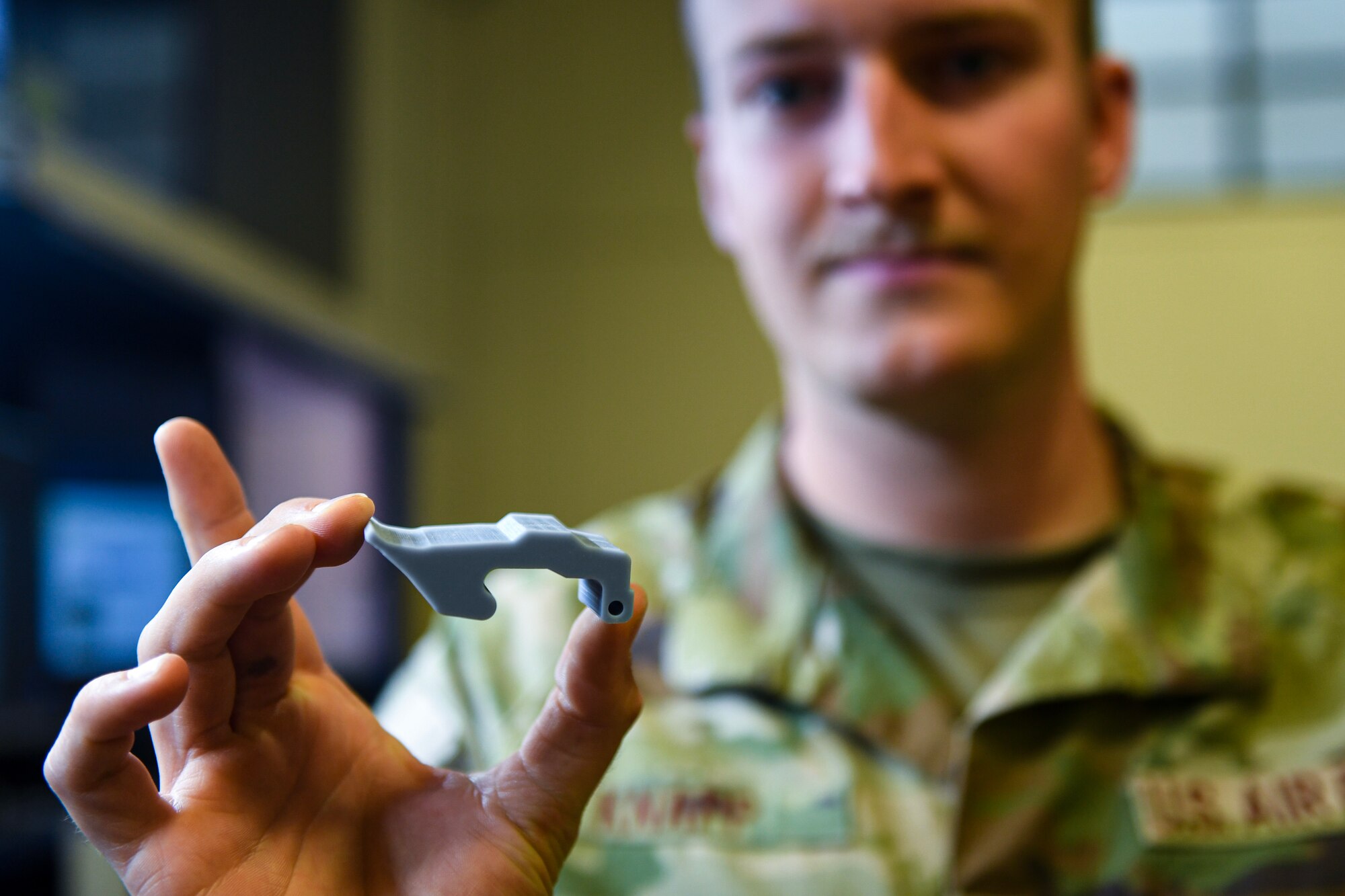 Air Force NCO holds up a 3-D printed toolbox latch