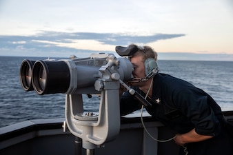 CT3 Ryan Regis uses the bridge wing binoculars to track forward contacts during a sea-and-anchor detail aboard USS Sterett (DDG 104) while in-transit to Manila, Philippines.