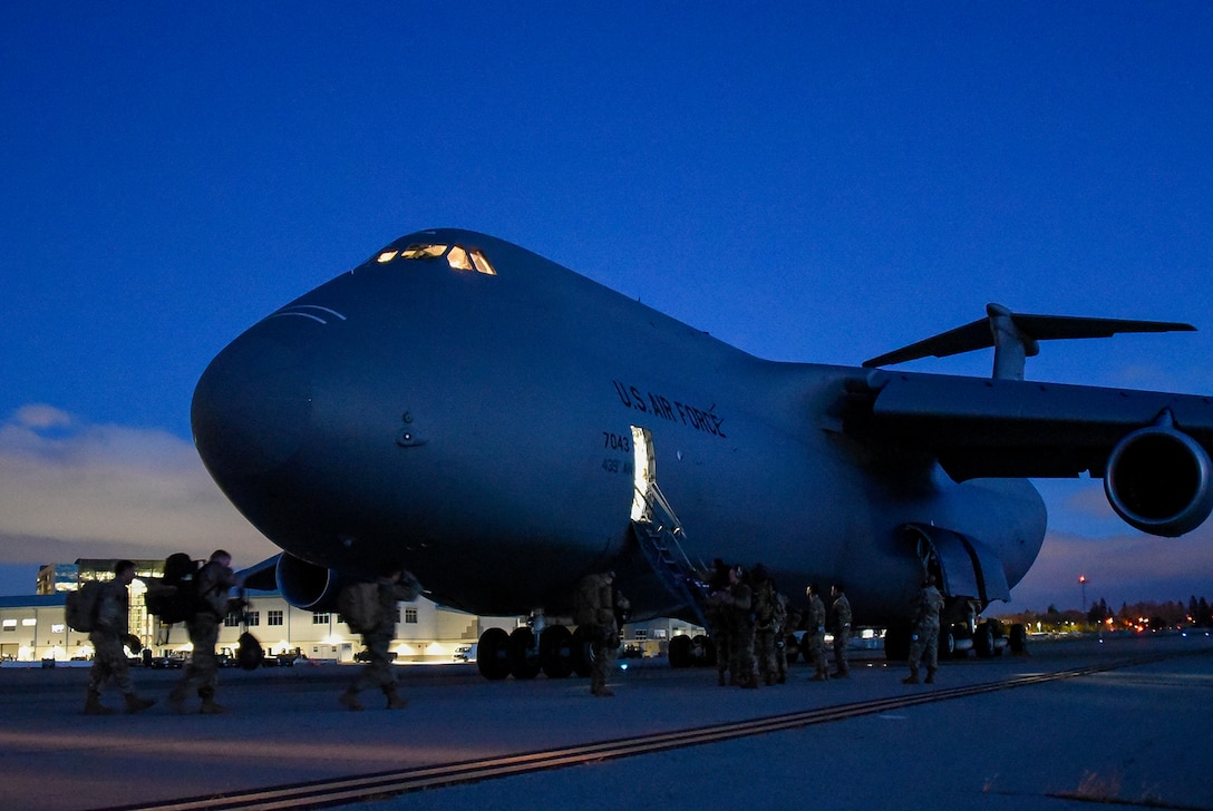 Airmen board a military aircraft at dusk.
