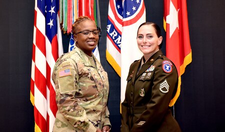Two female Soldiers pose together in front of an array of flags