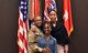 Female Soldier poses with an older and younger female in front of an array of flags