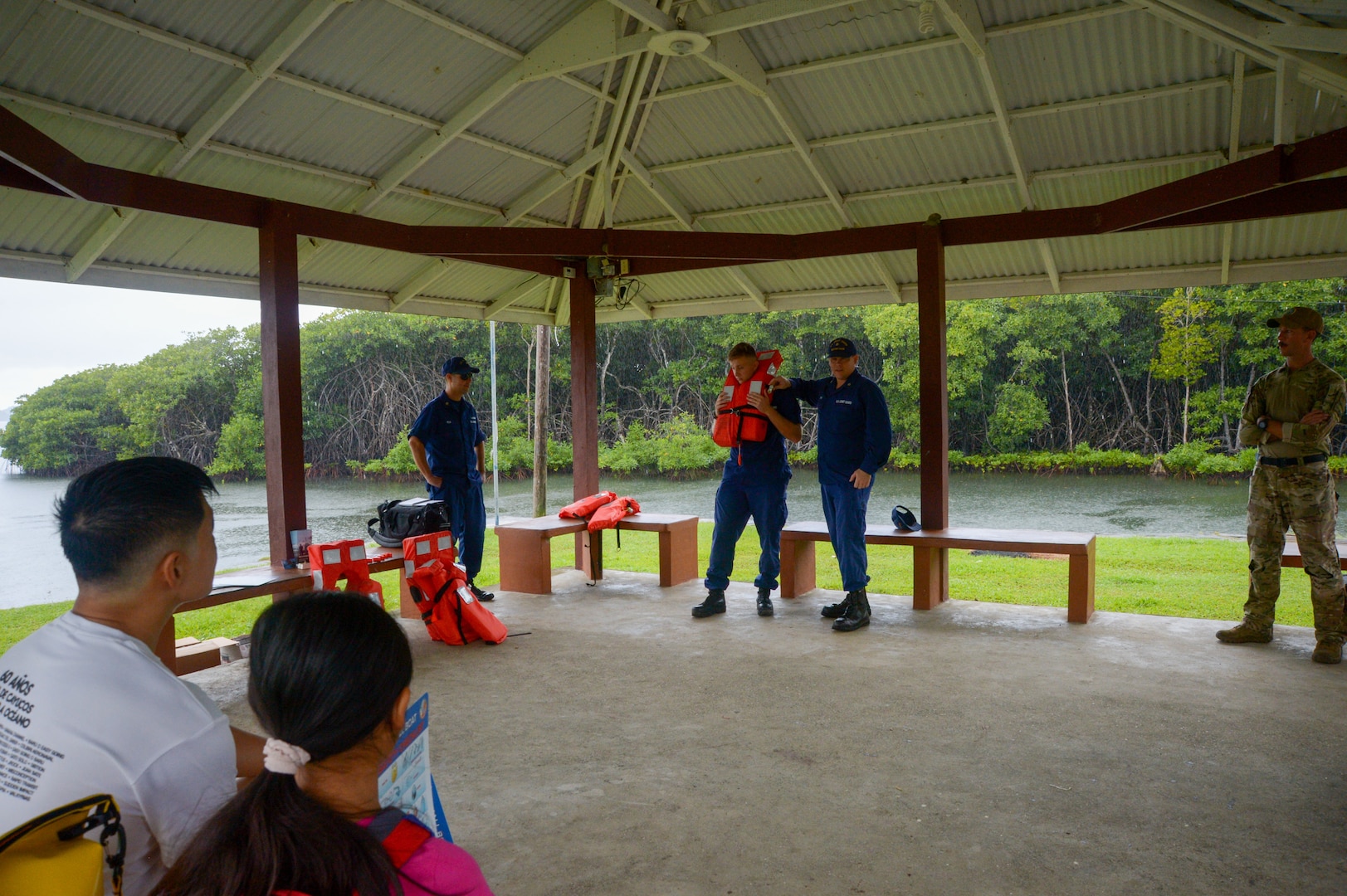 U.S. Coast Guard Marine Science Technician 2nd Class Benjamin Smits, from North Webster, Indiana, middle right, and Marine Science Technician 3rd Class Alexander Brenton, from Roanoke, Virginia, middle left, demonstrate how to wear a Type 1 personal flotation device for local Palauan residents during a boat safety class in Airai, Palau, as part of Pacific Partnership 2024-1, Dec. 28, 2023. Pacific Partnership, now in its 19th iteration, is the largest multinational humanitarian assistance and disaster relief preparedness mission conducted in the Indo-Pacific and works to enhance regional interoperability and disaster response capabilities, increase security stability in the region, and foster new and enduring friendships. (U.S. Navy photo by Mass Communication Specialist 2nd Class Jacob Woitzel)