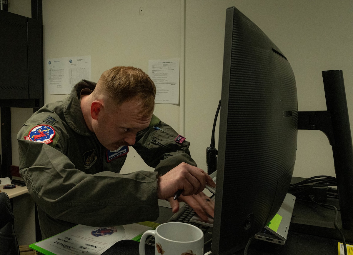 A man in uniform looks closely at computer screen in a office
