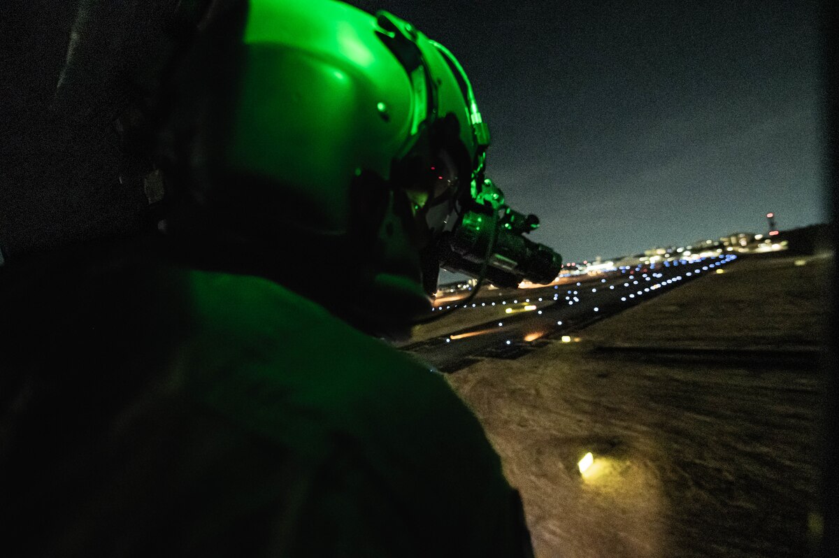 An Airman wearing a helmet and night vision goggles is looking out of a UH-1N Huey.