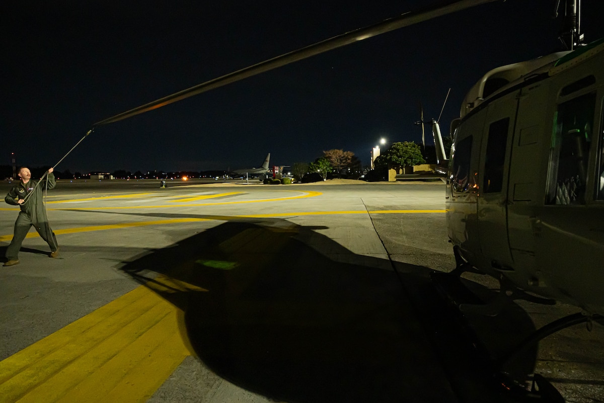 Airman in uniform helps prepare for UH-N1 Huey take off at night.