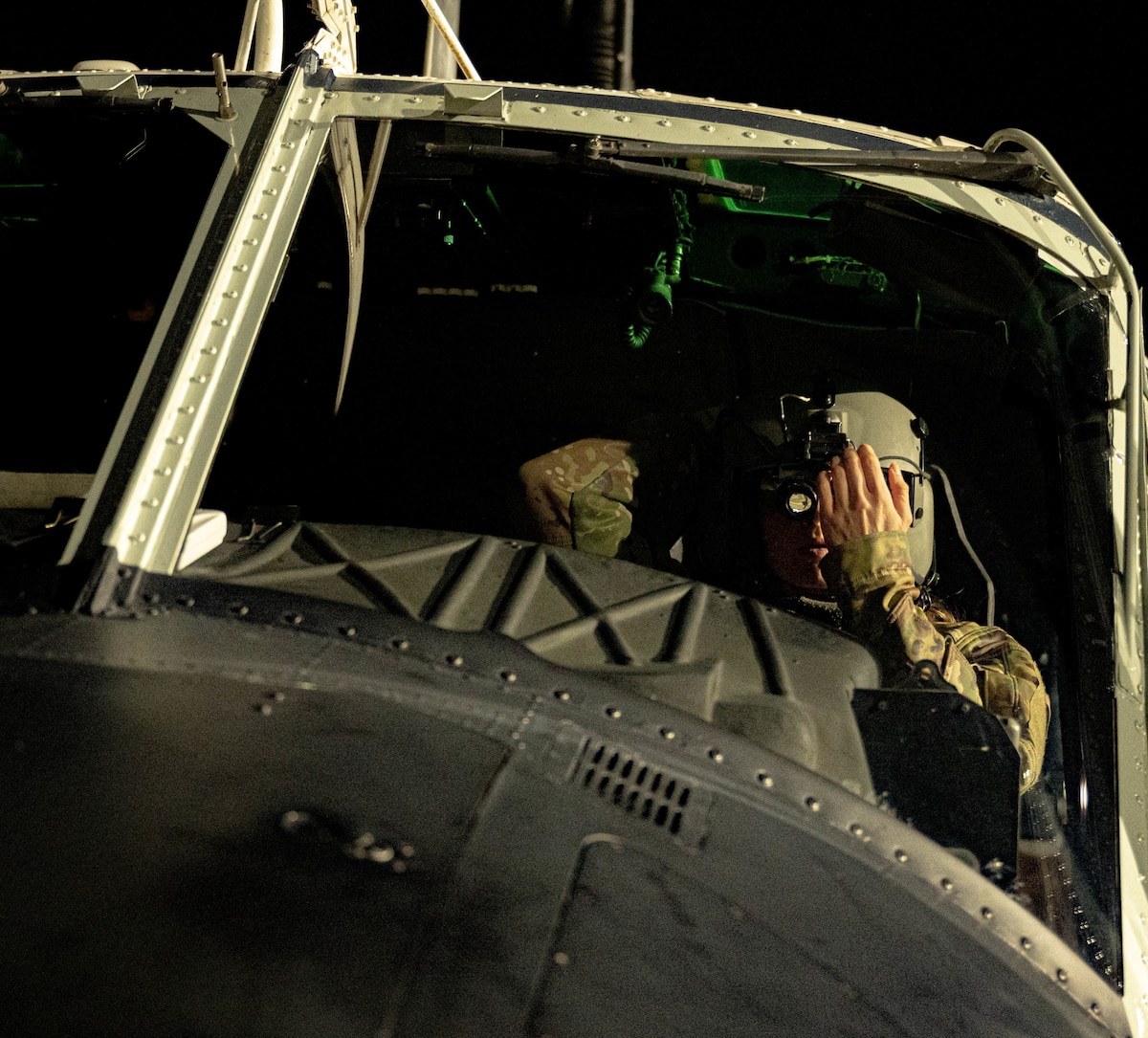 A pilot has their hand over their goggles in the cockpit of a UH-Huey.