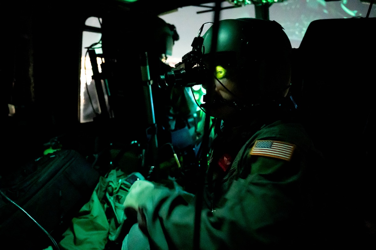 An Airman is sitting in a Huey wearing his uniform and visible by green lighting. His eye is brightened by the light of his night vision goggles.