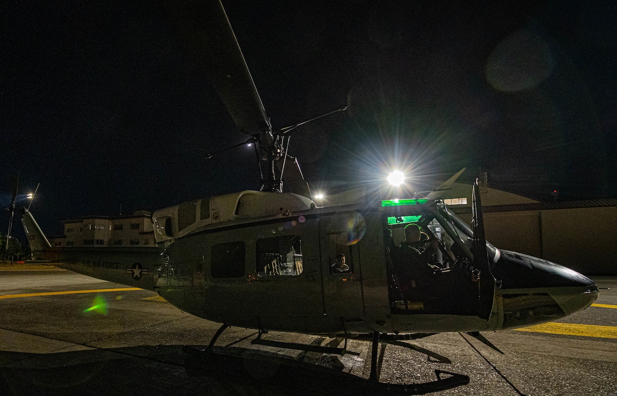A UH-N1 Huey is being prepared before take off at night. Three Airmen are inside checking their equipment.