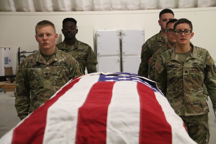 Soldiers stand next to a casket for funeral training.