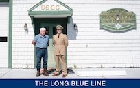 Two men pose together at parade rest in front of a U.S. Coast Guard Navigation Team building.