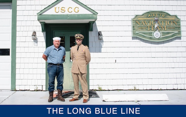 Two men pose together at parade rest in front of a U.S. Coast Guard Navigation Team building.