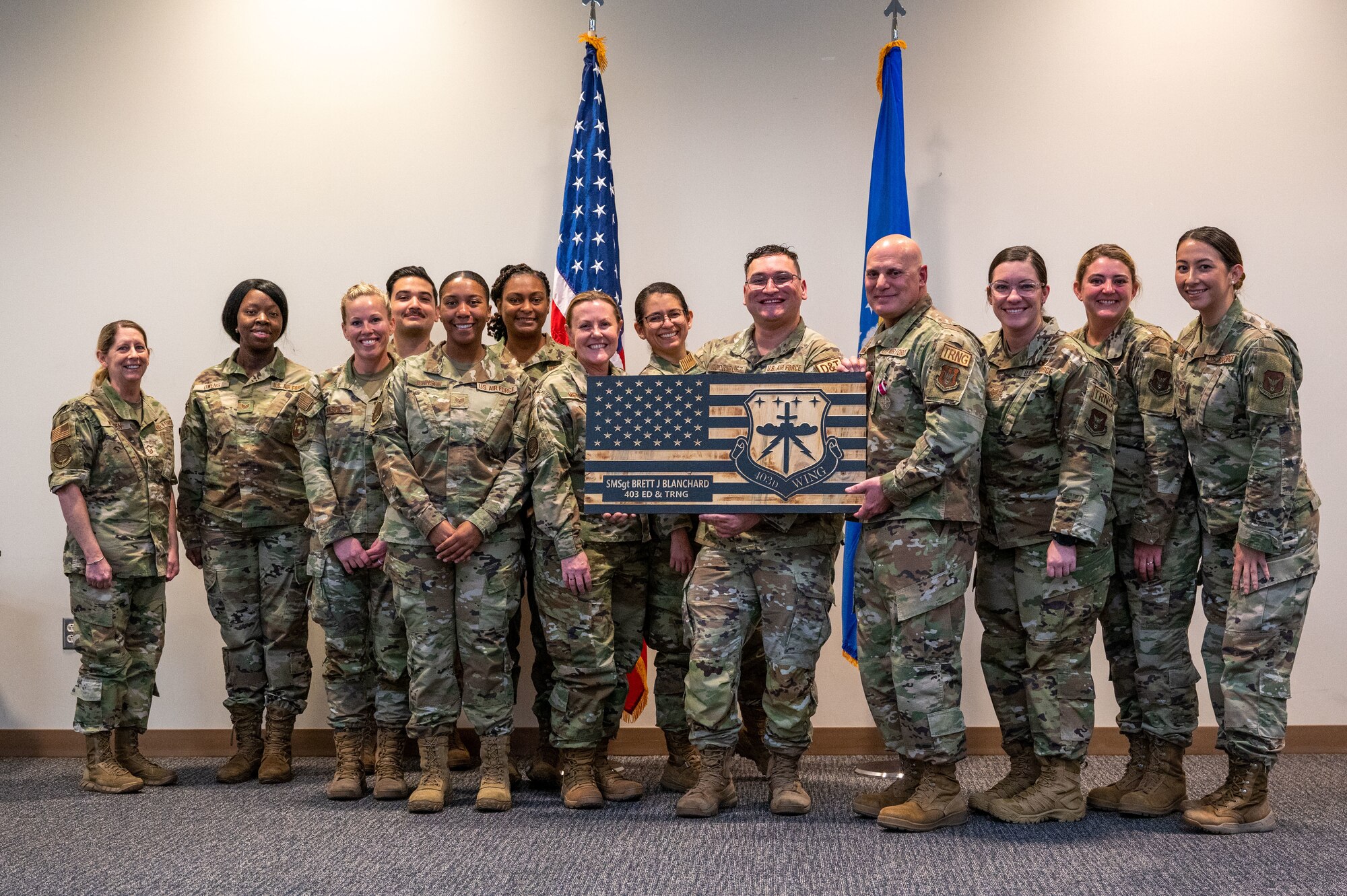 A group of airman stand together. Two hold a large wooden American flag