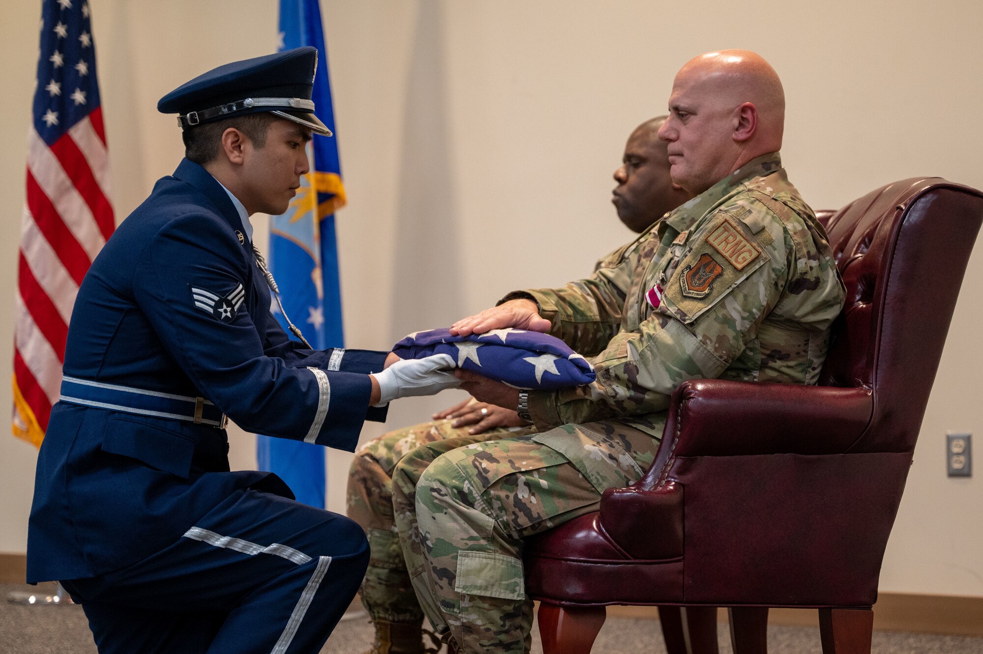 An Airman in service dress kneels to present Blanchard with a folded american flag