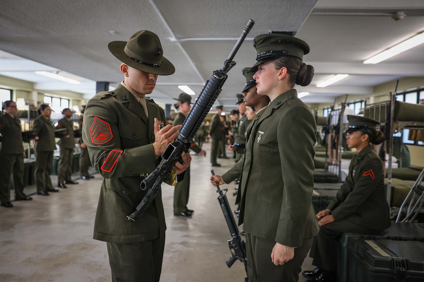 A Marine Corps officer inspects a weapon as recruits stand at attention.