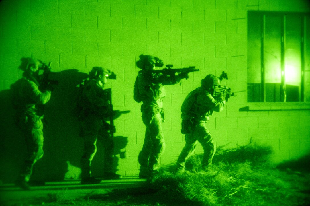Four sailors participate in nighttime training with weapons. They are illuminated by a green light.