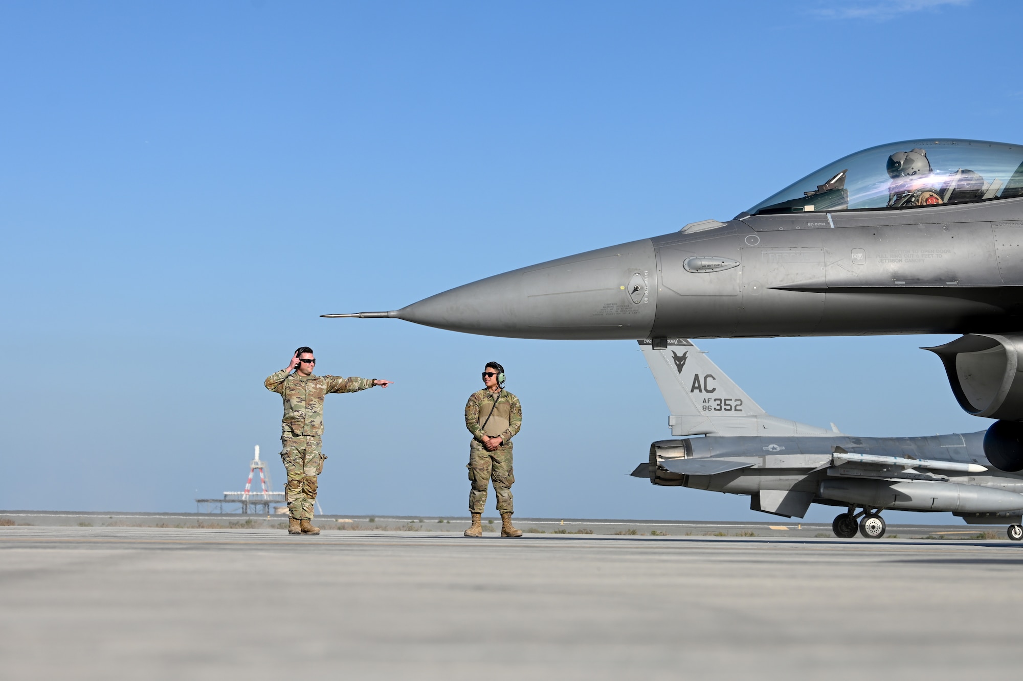 SrA Ortolani, right, watches as TSgt Bollock, a logistician, embodies the multi-capable Airman concept by marshaling a F-16 Fighting Falcon.