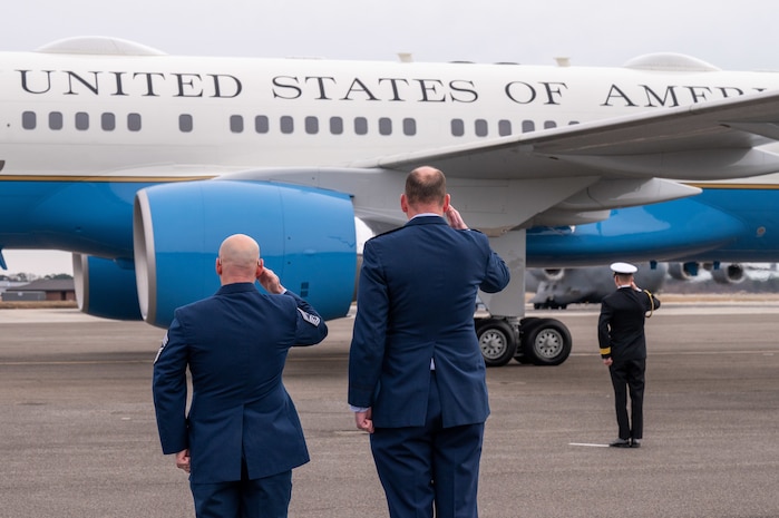 A photo of three men saluting at an aircraft.