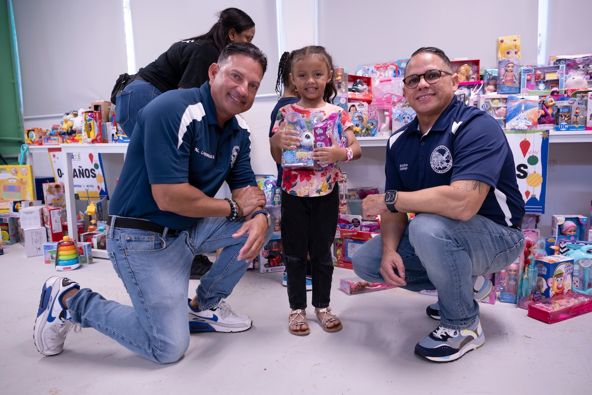 U.S. Air Force Chief Master Sgt. Chief Master Sgt. Neil Larregui, the state command chief, Puerto Rico Air National Guard, and Chief Master Sgt. Orlando Soto, the 156th Wing command chief, PRANG, pose for a photo with a child during a Three Kings eve event at Loiza, Puerto Rico, Jan. 5, 2024. For 48 consecutive years, the PRANG has honored a Puerto Rican tradition, Three Kings Day, by impacting the Piñones community through a yearly event where the 156th Wing Chiefs Council and U.S. Airmen partnered with local non-profit organizations to impact hundreds of children with ages ranging from newborn to 12-years-old, during the eve of Three Kings Day. (U.S. Air National Guard photo by Airman 1st Class Sharymel Montalvo Velez)