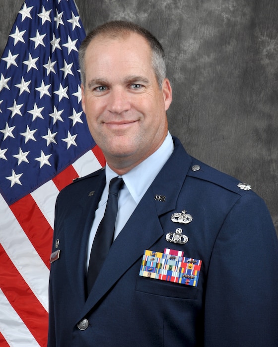 Photo of David Borden in U.S. Air Force dress uniform. Gray background with American flag behind him.