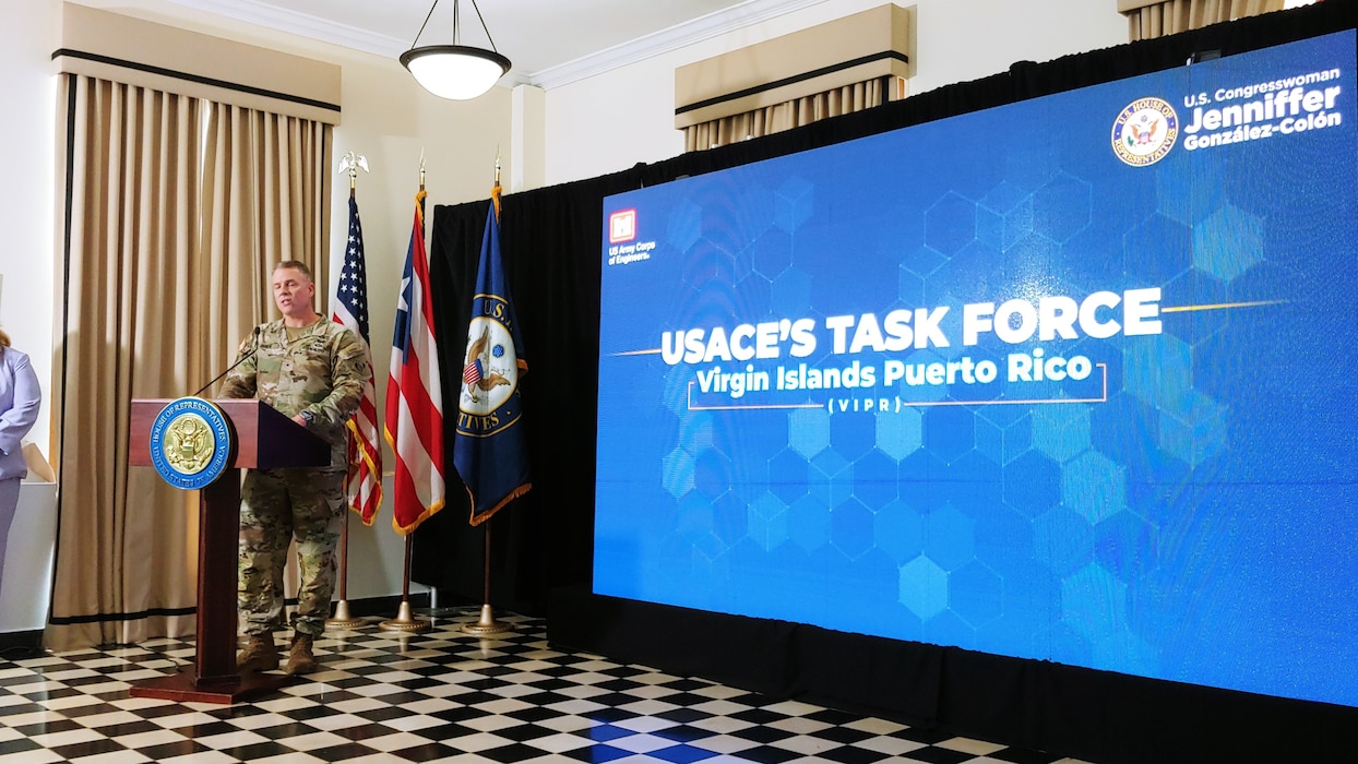 Brig. Gen Daniel Hibner in camouflage uniform speaking in front of a podium.