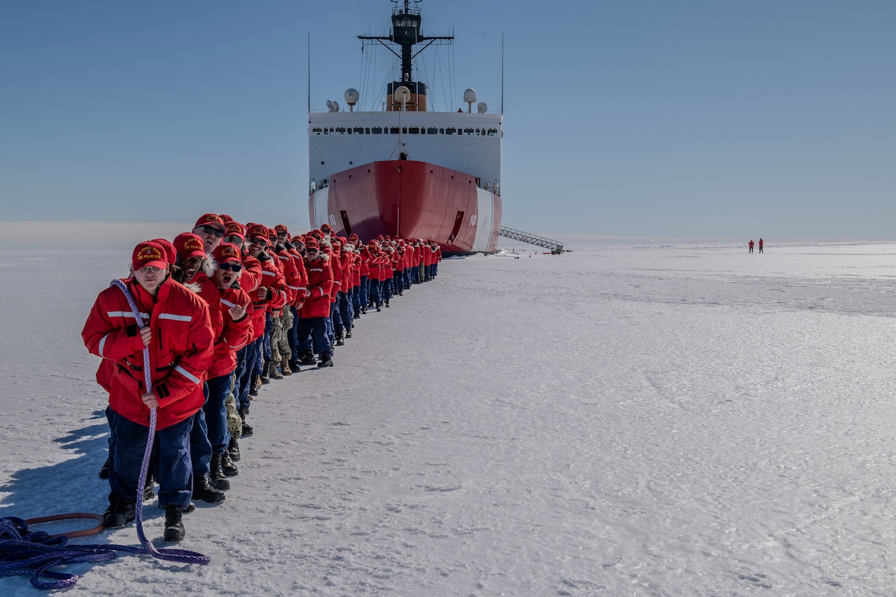 A group of Coast Guard members mimic towing a vessel on Antarctic ice using a rope.