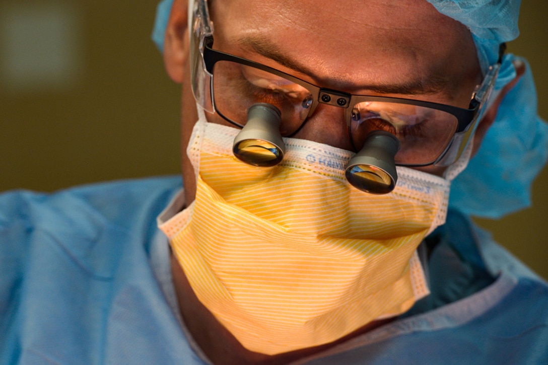Close-up of a physician wearing surgical loupes, a scrub cap and a surgical mask.