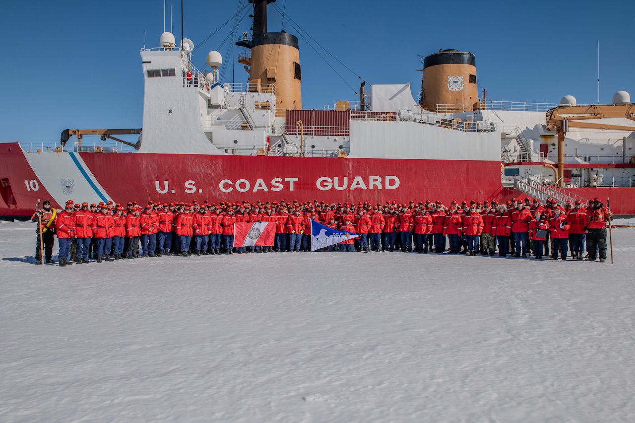 A large group of Coast Guard members stand in front of a cutter on ice.