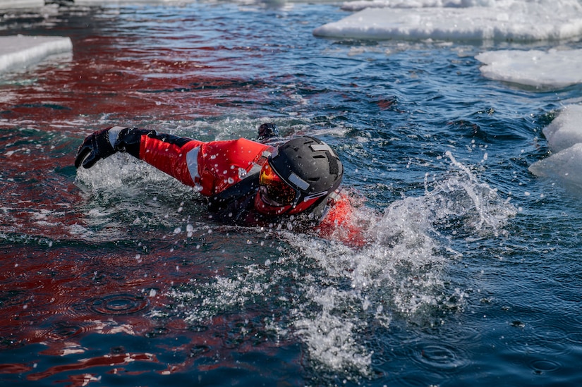 A Coast Guard member swims in icy water during rescue training.