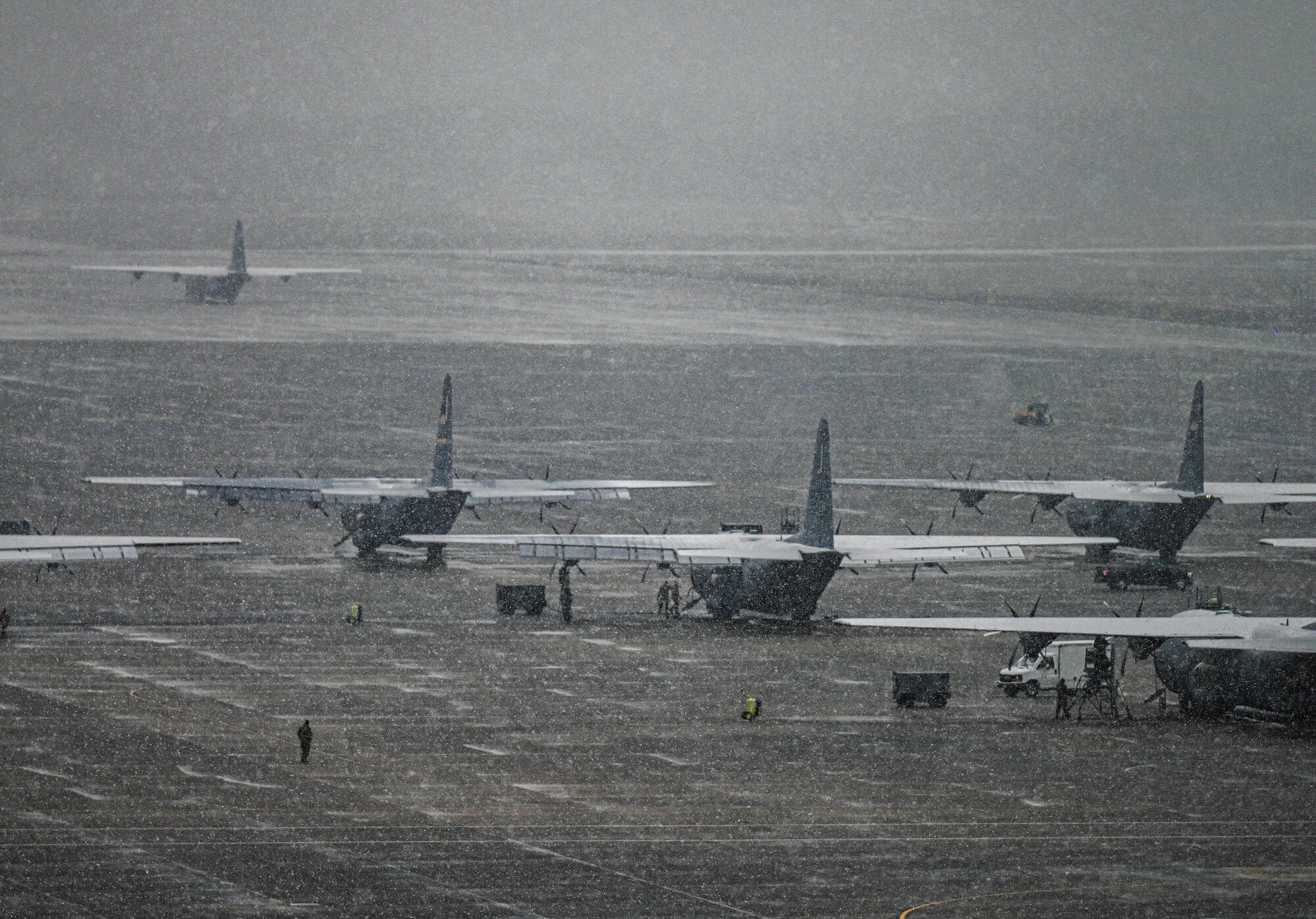A row of military aircraft sit parked and covered in snow.
