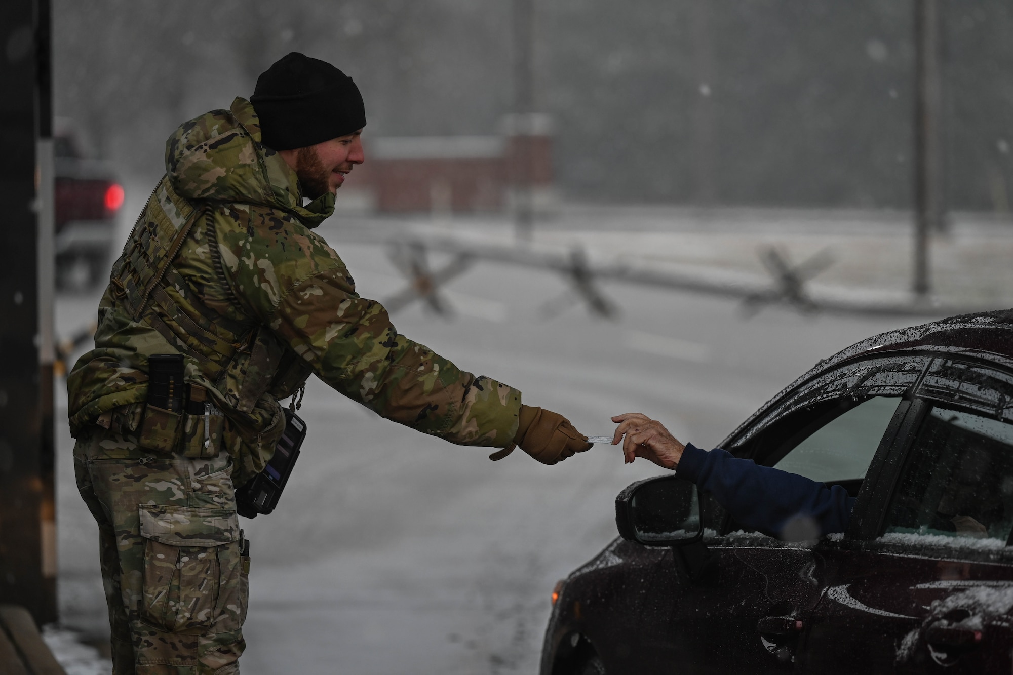 A man in uniform hands a driver their common access card back to them at the gate of a military instillation.